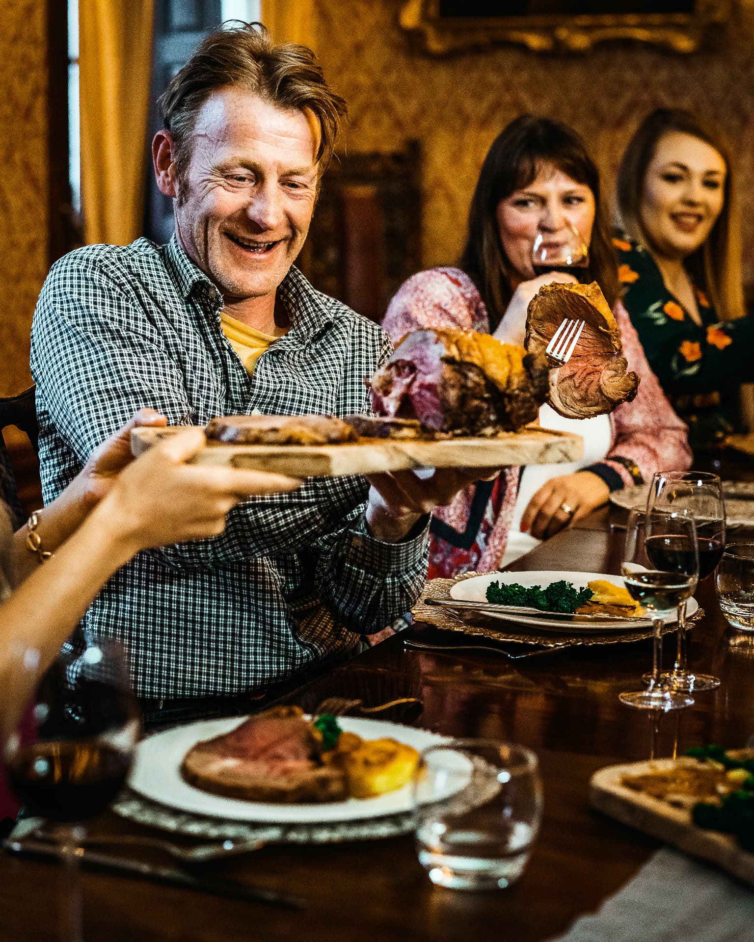 A guest smiling as roast meat is passed across the dinner table